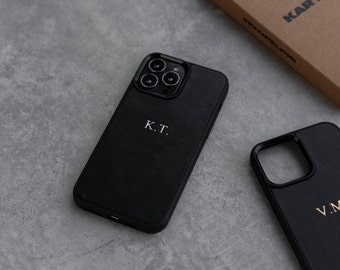 May include: Two black leather phone cases with personalized initials. The case on the left has the initials "K.T." and the case on the right has the initials "V.M."