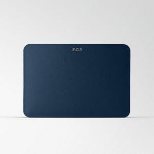 Puede incluir: Un clutch de cuero azul oscuro con las iniciales "F.G.Y." grabadas en oro.