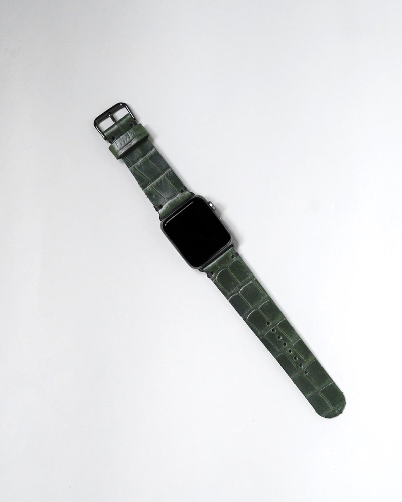 May include: A dark green leather watch band with a crocodile pattern. The band is attached to a black smartwatch with a black screen.