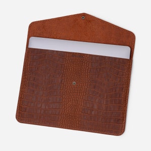 May include: Brown leather laptop sleeve with a crocodile pattern. The sleeve is open and a laptop is inside.