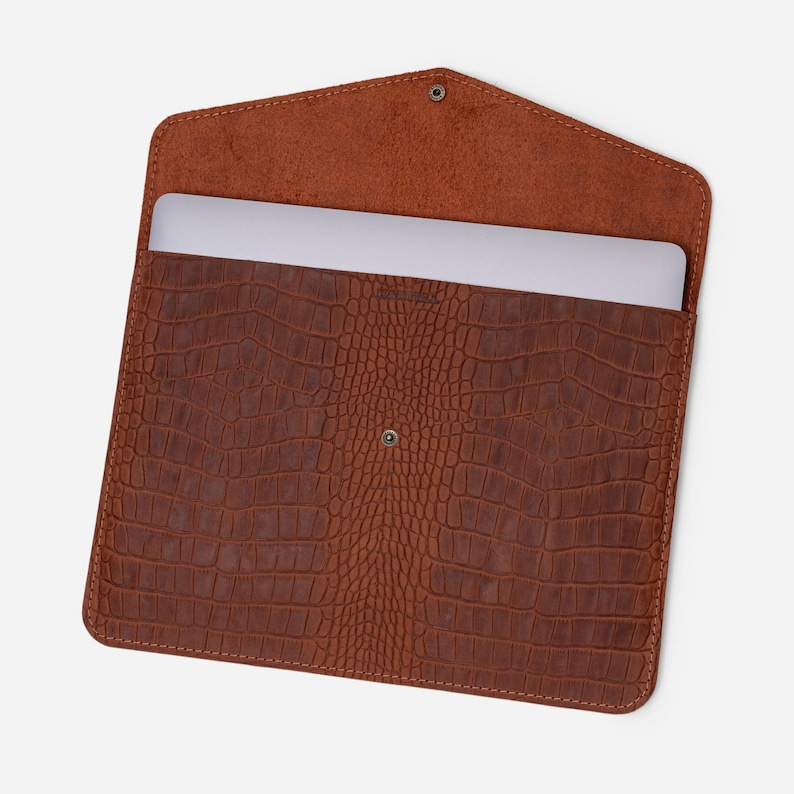 May include: Brown leather laptop sleeve with a crocodile pattern. The sleeve is open and a laptop is inside.