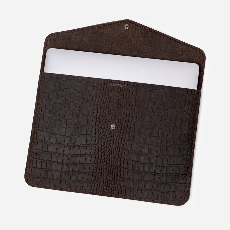 May include: Brown leather laptop sleeve with a crocodile embossed pattern. The sleeve is open and a laptop is visible inside.