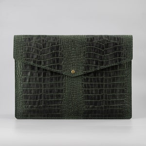 May include: A dark green leather envelope with a crocodile embossed pattern and a gold button closure.