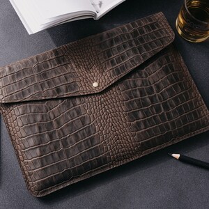 May include: A brown leather envelope clutch with a crocodile embossed pattern and a gold button closure.
