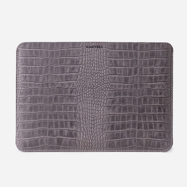 K&ouml;nnte beinhalten: Graue Ledertasche f&uuml;r Laptops mit Kroko-Muster und dem gepr&auml;gten Schriftzug "KARTELL" auf der Vorderseite.