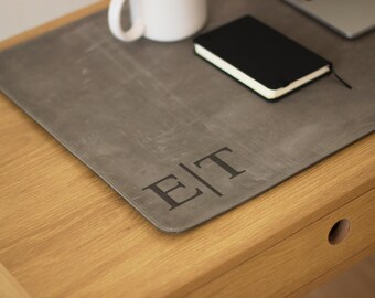May include: A gray leather desk mat with the initials "E|T" embossed on the surface. The mat is on a wooden desk with a drawer.