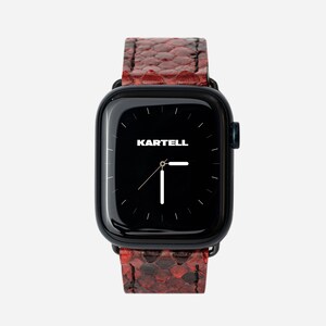 Op de afbeelding: Een zwarte smartwatch met een rood slangenleren bandje. De wijzerplaat van het horloge is zwart met witte wijzers en het woord "KARTELL" staat in wit gedrukt.