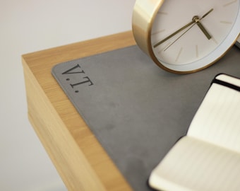 May include: A gray leather desk mat with the initials "V.T." embossed on it. A gold clock and a notebook are on the mat.