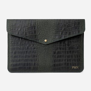 May include: A dark green leather laptop sleeve with a crocodile embossed pattern and a gold button closure. The sleeve has the initials "PHN" embossed on the bottom right corner.