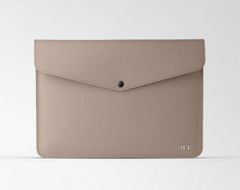 Puede incluir: Un clutch de sobre de cuero marrón claro con cierre de presión y las iniciales "JLT" grabadas en la parte delantera.