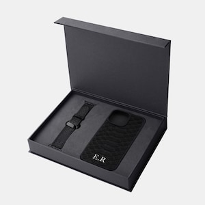 以下が含まれることがあります： 黒いギフトボックスの中に、黒い革製の携帯電話ケースと黒い革製の腕時計バンドが入っています。携帯電話ケースには「E.R.」のイニシャルが刻印されています。