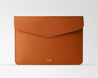 Puede incluir: Una funda para portátil de cuero marrón de estilo sobre con las iniciales "LW" grabadas en plata en la parte delantera.