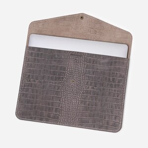May include: Gray leather laptop sleeve with a crocodile embossed pattern. The sleeve is open and a laptop is visible inside.