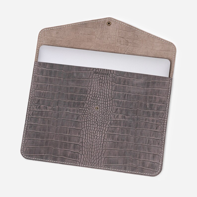 May include: Gray leather laptop sleeve with a crocodile embossed pattern. The sleeve is open and a laptop is visible inside.