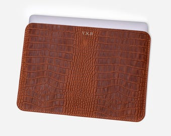 May include: A brown leather laptop sleeve with a crocodile pattern and the initials "V.K.B." embossed on the front.