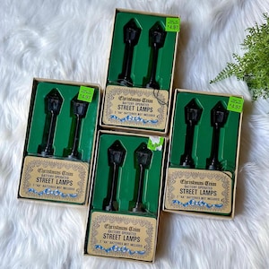 May include: Five packages of battery operated street lamps. Each package contains two black street lamps with a gold top. The packages are brown with green and gold accents. The packages have a price tag of $4.97. The text on the packages reads "Christmas Crim Battery Operated Street Lamps 2 "AA" Batteries Not Included."