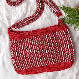 Pode incluir: Bolsa vermelha de crochê com uma alça de corrente prateada feita de abas de latas de alumínio recicladas.