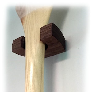 May include: A wooden paddle holder with two dark brown wooden brackets. The paddle holder is mounted on a white wall.
