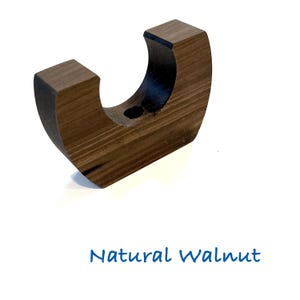 May include: A U-shaped dark brown wooden holder with a smooth finish and visible wood grain. The object features a central circular opening at the base of the curve. The text Natural Walnut is printed in blue below the wooden object.