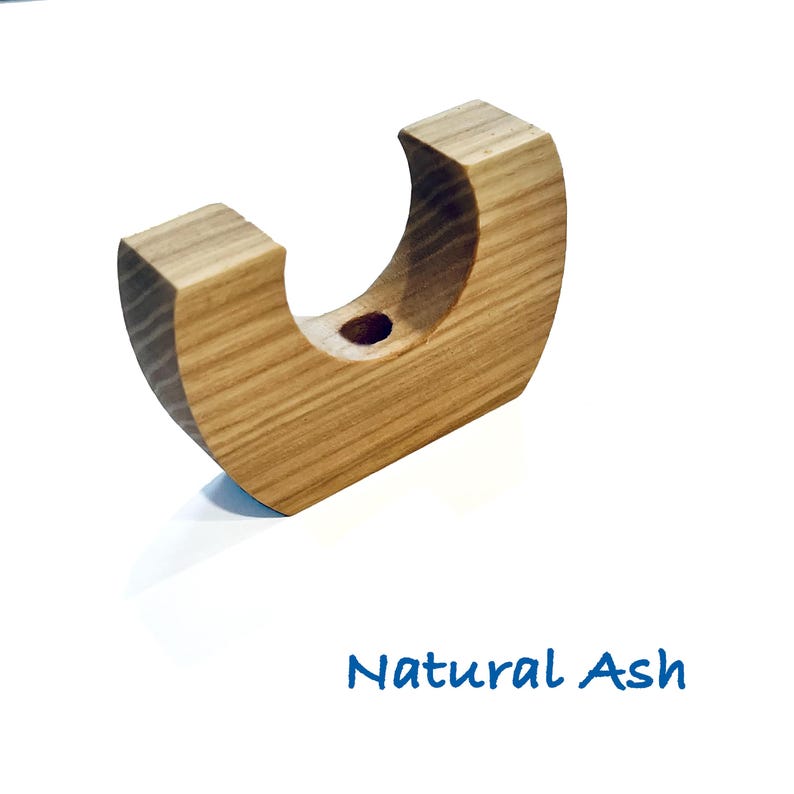 May include: A U-shaped natural ash wood object with a smooth, light brown grain pattern and a small circular hole centered at the base of the curve. The text Natural Ash is printed in blue below the wooden item on a plain white background.
