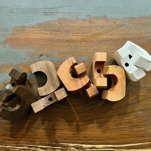 May include: A collection of six C-shaped wooden components in varying shades of brown, tan, and white. Each piece features a smooth, curved exterior, a flat interior edge, and a small circular hole drilled through the center of the structure.