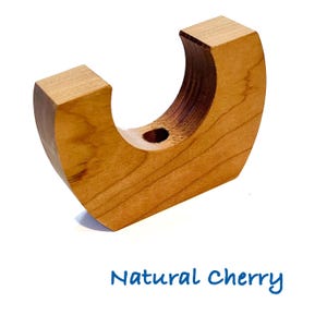 May include: A crescent-shaped natural cherry wood holder with a smooth finish and a circular cutout at the top center. The object features a light brown wood grain pattern and is labeled with the blue text Natural Cherry below the item.