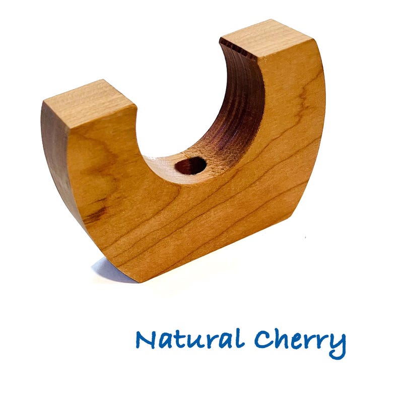 May include: A crescent-shaped natural cherry wood holder with a smooth finish and a circular cutout at the top center. The object features a light brown wood grain pattern and is labeled with the blue text Natural Cherry below the item.