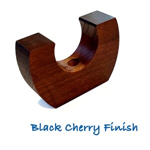 May include: A crescent-shaped wooden candle holder with a smooth, dark brown finish. The object features a central circular opening for a candle and is labeled with the text Black Cherry Finish below the base on the white background.
