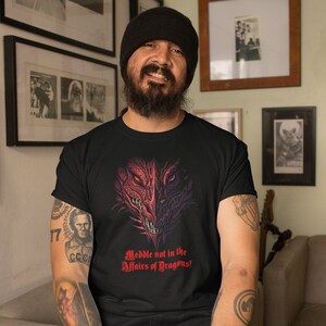 May include: A black t-shirt with a graphic of a red and purple dragon head. The text "Meddle not in the Affairs of Dragons!" is printed below the dragon head.
