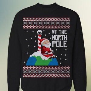 May include: Black Christmas jumper with a white and red patterned design. Santa Claus is sitting on a globe with a candy cane pole behind him. The text "WE THE NORTH POLE" is printed on the jumper.