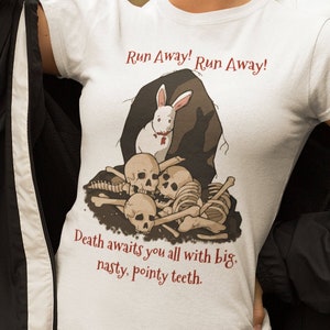 May include: White t-shirt with a graphic of a white rabbit with red eyes standing on a pile of bones. The text "Run Away! Run Away!" is above the rabbit and the text "Death awaits you all with big, nasty, pointy teeth." is below the rabbit.