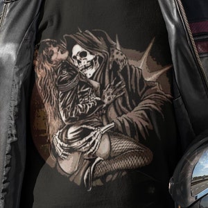 May include: A black t-shirt featuring a graphic print of a skeleton holding a woman. The skeleton is wearing a hooded robe and the woman is wearing a black dress and fishnet stockings. The graphic is in shades of grey and brown.