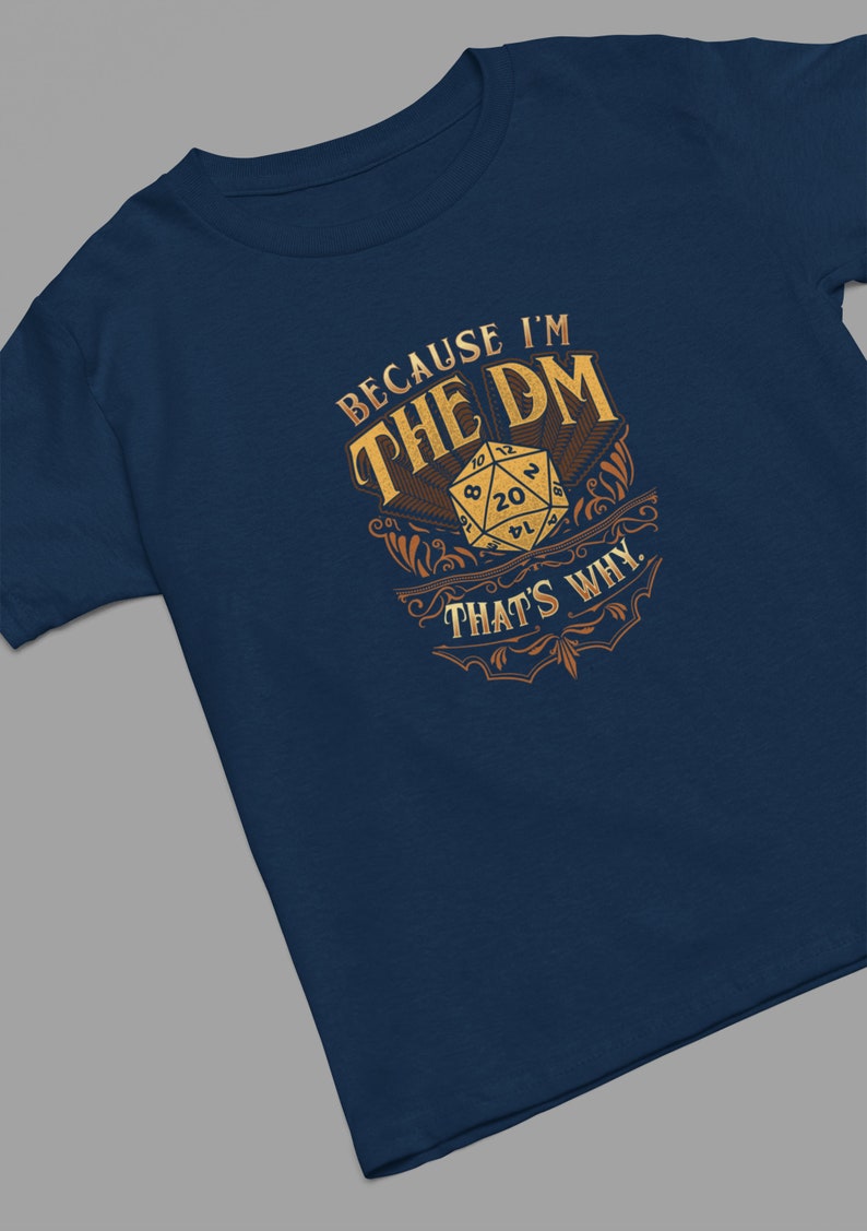 May include: A navy blue t-shirt with a gold design featuring a 20-sided die and the text "Because I'm the DM That's Why."