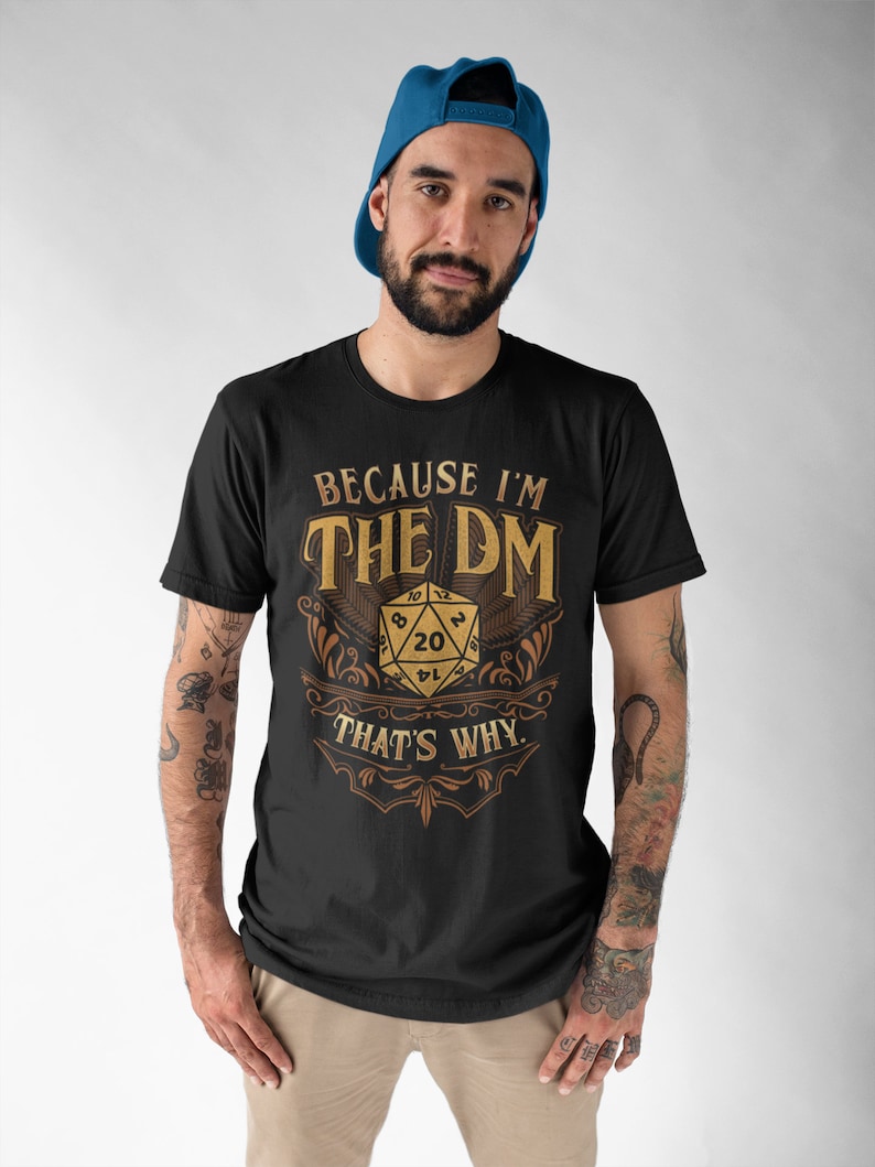 May include: A black t-shirt with a gold design featuring a 20-sided die and the text "Because I'm The DM That's Why."