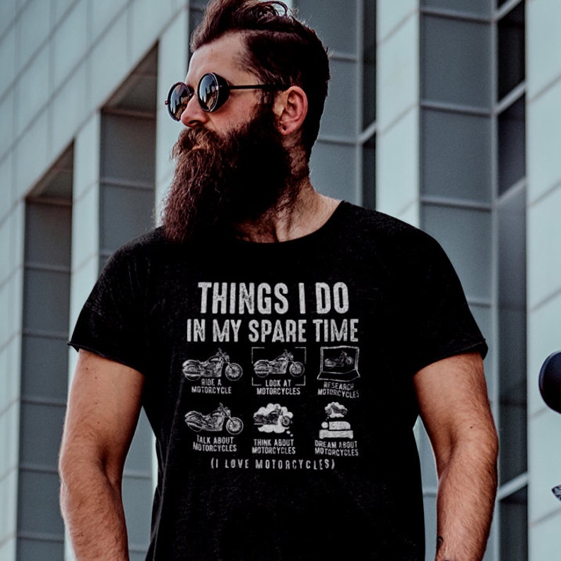 May include: A black t-shirt with white text that reads "Things I do in my spare time" and lists activities related to motorcycles. The activities include riding, looking at, researching, talking about, thinking about, and dreaming about motorcycles. The text also includes the phrase "I love motorcycles".
