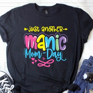 May include: Black t-shirt with the text "Just another manic mom-day" in colorful bubble letters with hearts and a swirl design.