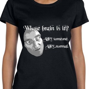 May include: Black t-shirt with a white graphic of a man's face and the text "Whose brain is it? Abby someone. Abby...normal."