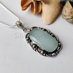 May include: A silver pendant necklace with a light blue oval gemstone set in a silver filigree frame. The pendant is on a silver chain.