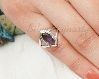 May include: A silver ring with a marquise-shaped amethyst gemstone. The ring has a delicate, open design with a silver band that wraps around the stone.