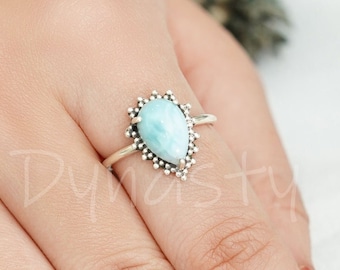 May include: A silver ring with a teardrop-shaped blue and green gemstone set in a silver halo design.
