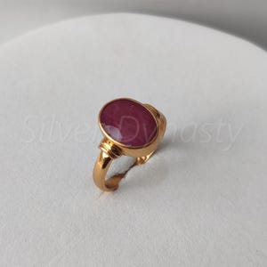 May include: A gold ring with a large oval-shaped ruby gemstone. The ring has a simple design with a smooth band.