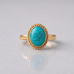 May include: A gold ring featuring an oval-shaped turquoise gemstone with dark veining. The stone is set within a twisted rope-style metal border, mounted on a smooth, polished gold band that completes the circular design of the jewelry piece.