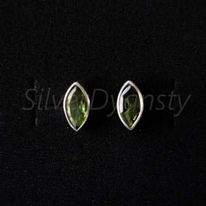 May include: A pair of silver earrings with green gemstone accents. The earrings are shaped like a teardrop and have a polished finish.