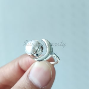 May include: A silver ring with a white pearl set in a crescent moon design.