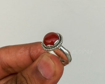May include: A silver ring with a red carnelian gemstone. The ring has a twisted band and a decorative setting around the stone.