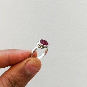 May include: A silver ring with a deep red gemstone set in a bezel setting.
