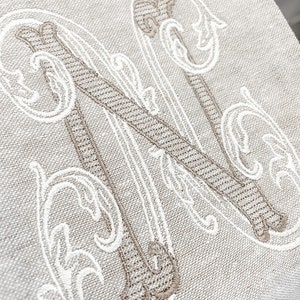May include: A white linen cushion with a large embroidered letter N in a brown and white script font.