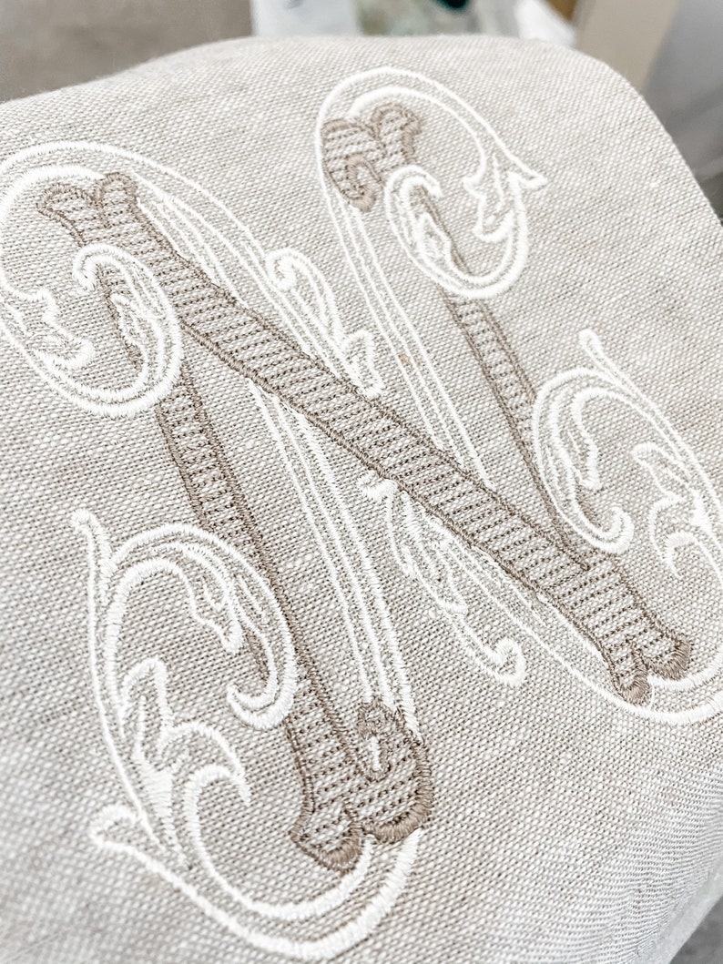 May include: A white linen cushion with a large embroidered letter N in a brown and white script font.