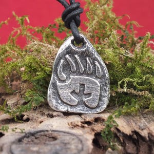 Op de afbeelding: Een zilveren berenpoot hangerketting met een zwart leren koord. De hanger is een gedetailleerd, gestructureerd ontwerp van een berenpootafdruk.