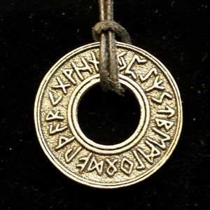 May include: Silver pendant necklace with a circular charm featuring a ring and runes around the edge. The pendant is attached to a black leather cord.